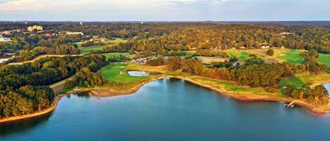 Vista aérea de un campo de golf con un lago grande, rodeado de bosques densos y zonas residenciales.