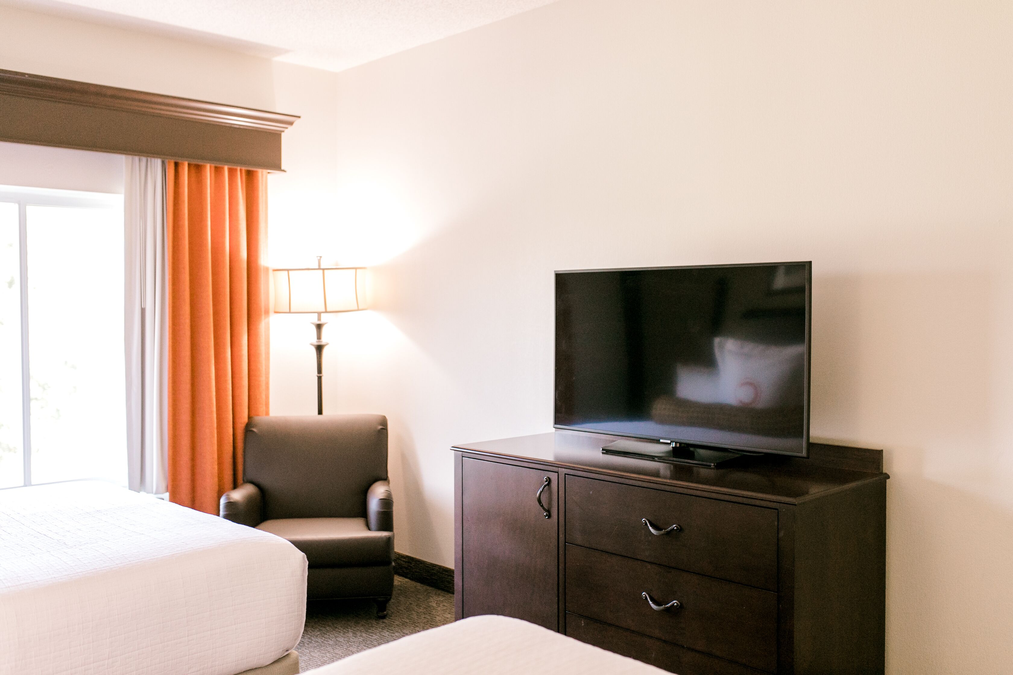 A hotel room with a bed, a chair, a TV on a cabinet, and a lamp.