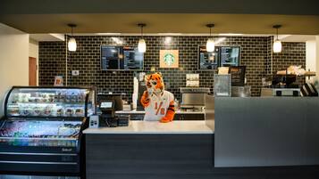 A Starbucks coffee shop interior with a tiger mascot, a menu board, a coffee machine, and a refrigerated display case.