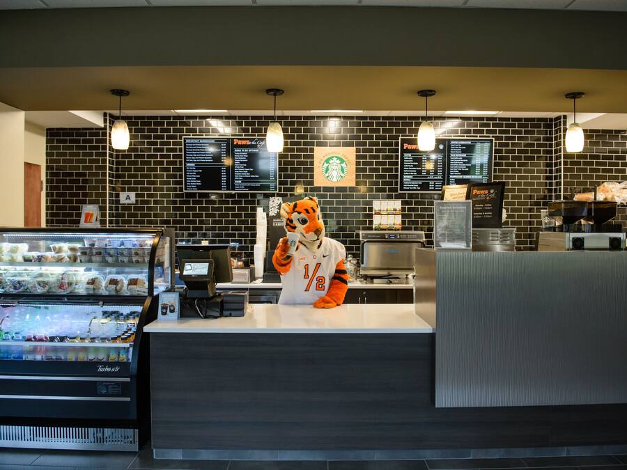 A Starbucks coffee shop interior with a tiger mascot, a menu board, a coffee machine, and a refrigerated display case.