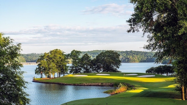 Campo de golf con un cuerpo de agua, árboles y una vista distante de un puente.