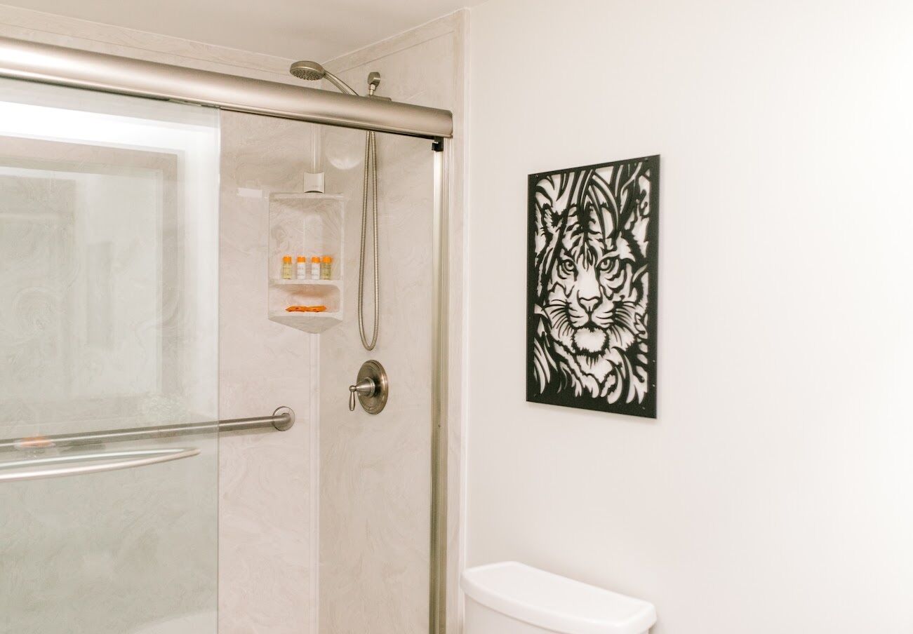 A bathroom with a glass shower enclosure, a toilet, and a wall-mounted artwork of a tiger.