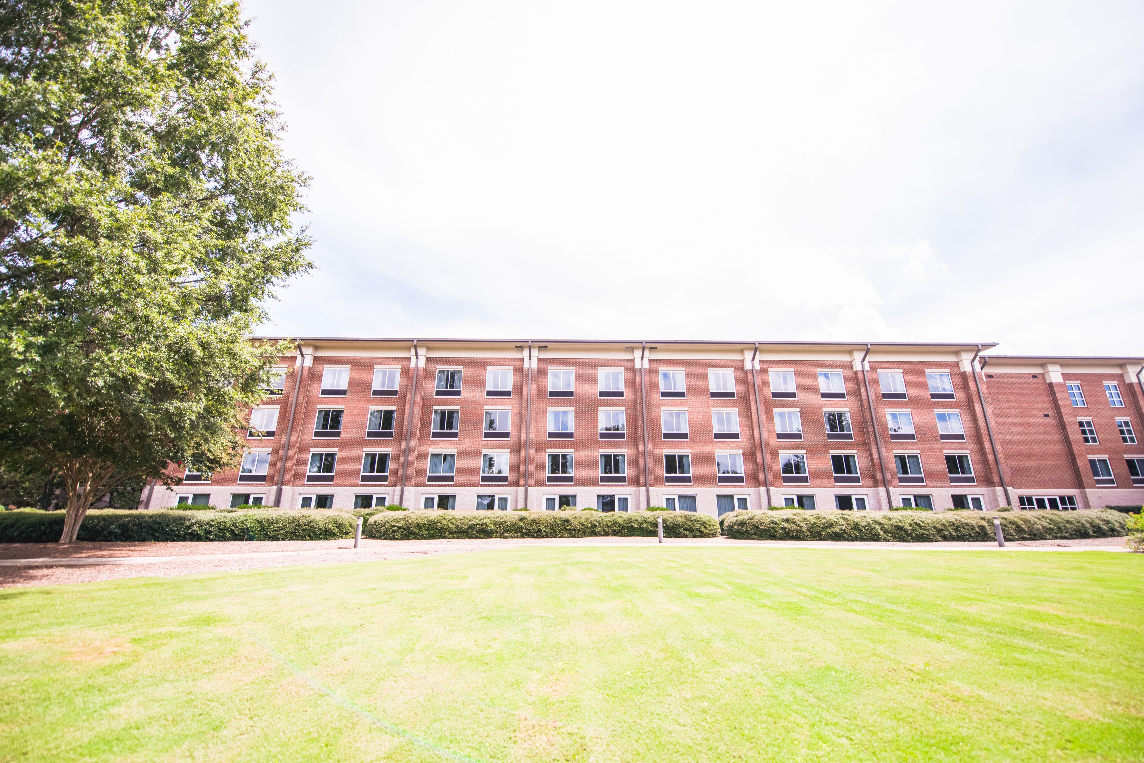A multi-story brick building with a flat roof, large windows, and a well-maintained lawn in front.
