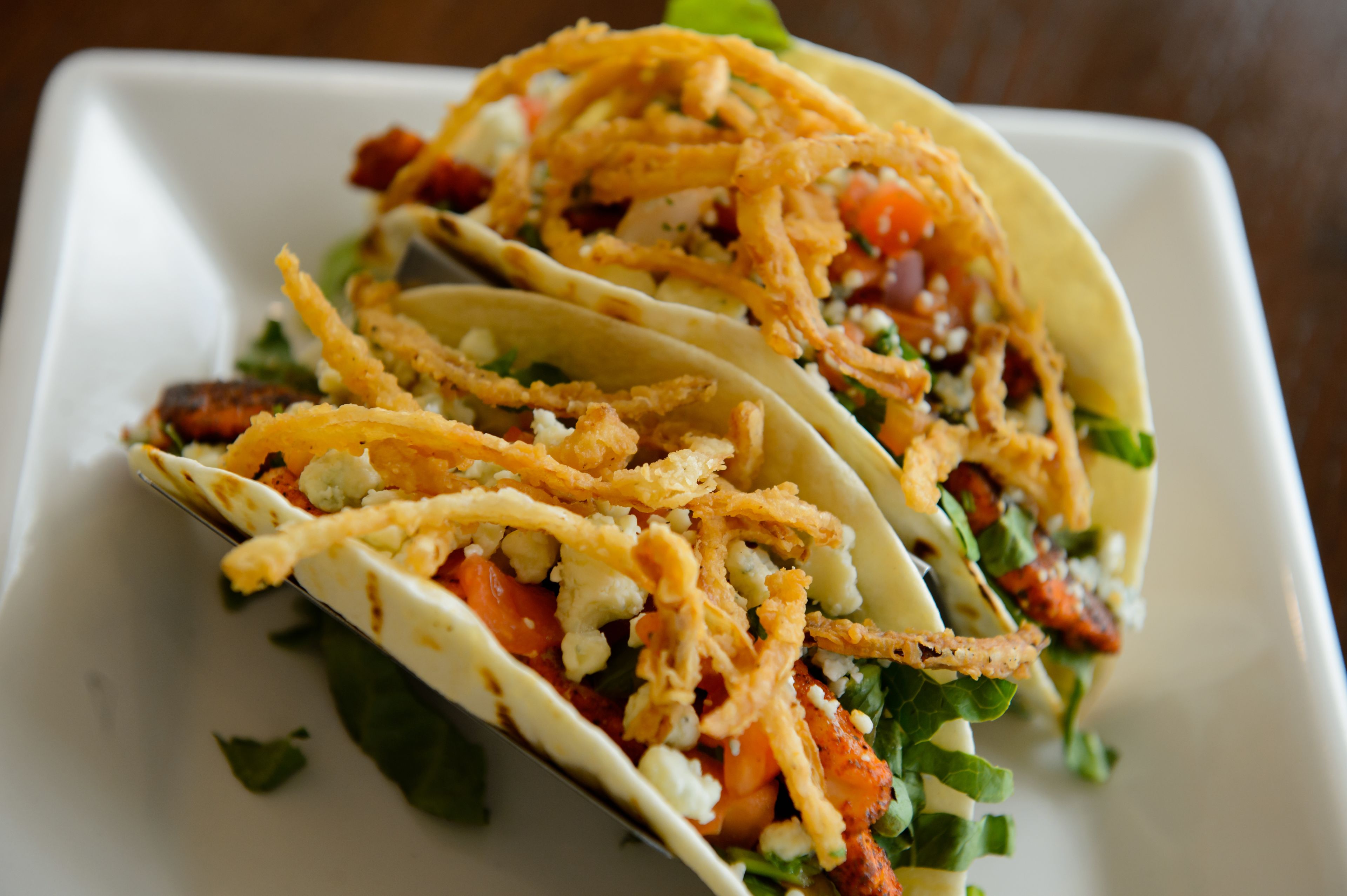 Three tacos with crispy toppings on a white plate.