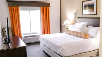 A hotel room with a large bed, a desk, a lamp, and a picture on the wall.