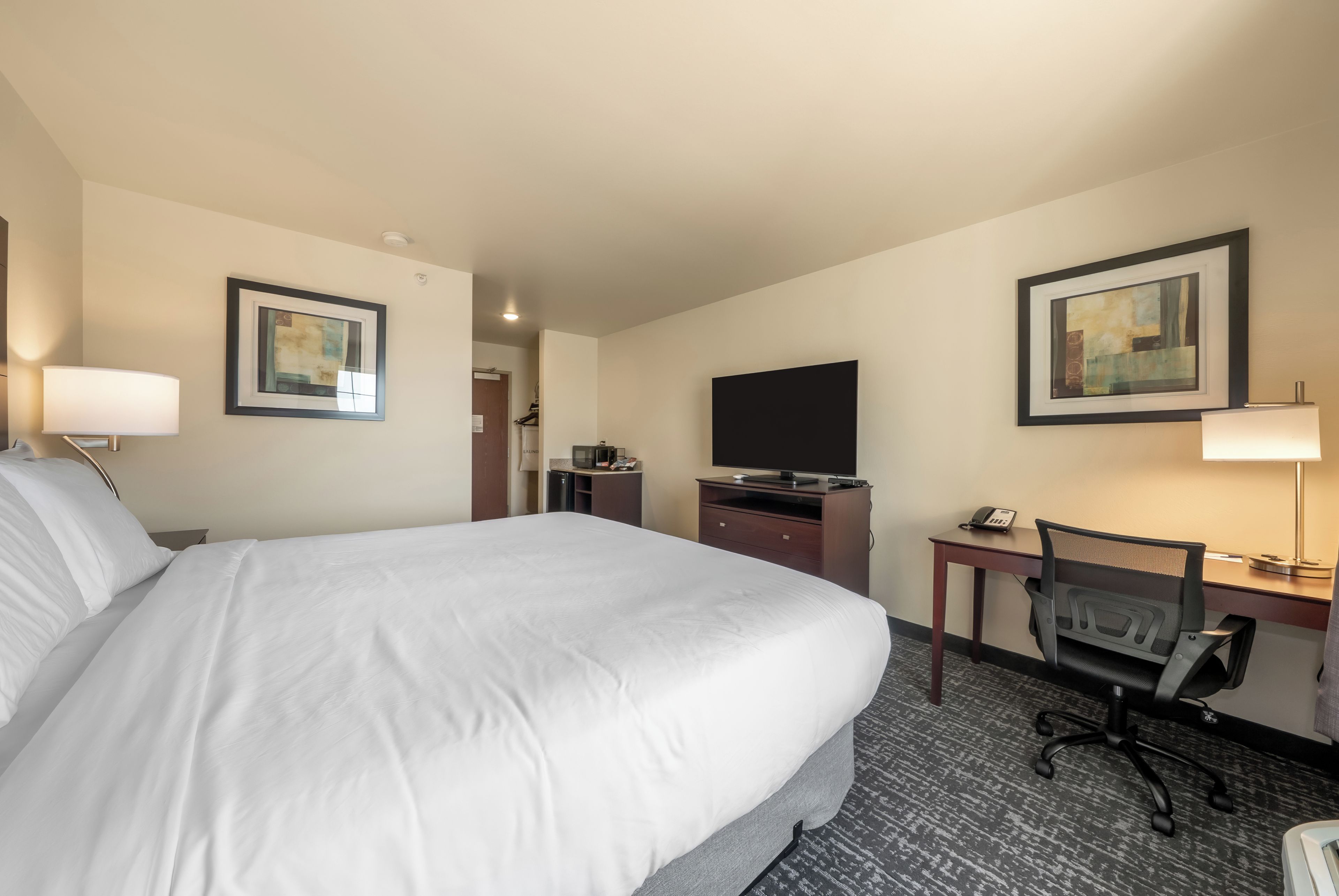 A hotel room with a large bed, a desk with a computer, a chair, a television, and artwork on the walls.
