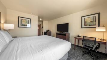 A hotel room with a large bed, a desk with a computer, a chair, a television, and artwork on the walls.