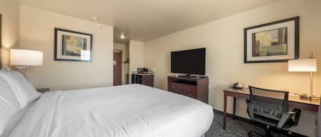 Una habitación de hotel con una cama grande, un escritorio con computadora, una silla, televisor y obras de arte en las paredes.