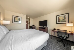 A hotel room with a large bed, a desk with a computer, a chair, a television, and artwork on the walls.