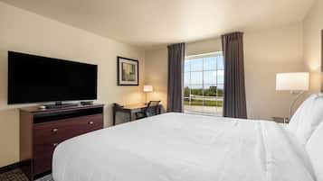 A hotel room with a bed, a desk with a chair, a television, a lamp, and a window with curtains.