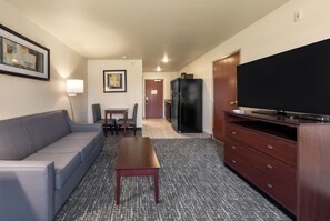 Habitación de hotel con sofá, una mesa, un televisor, un refrigerador y una puerta que da a una zona de cocina.