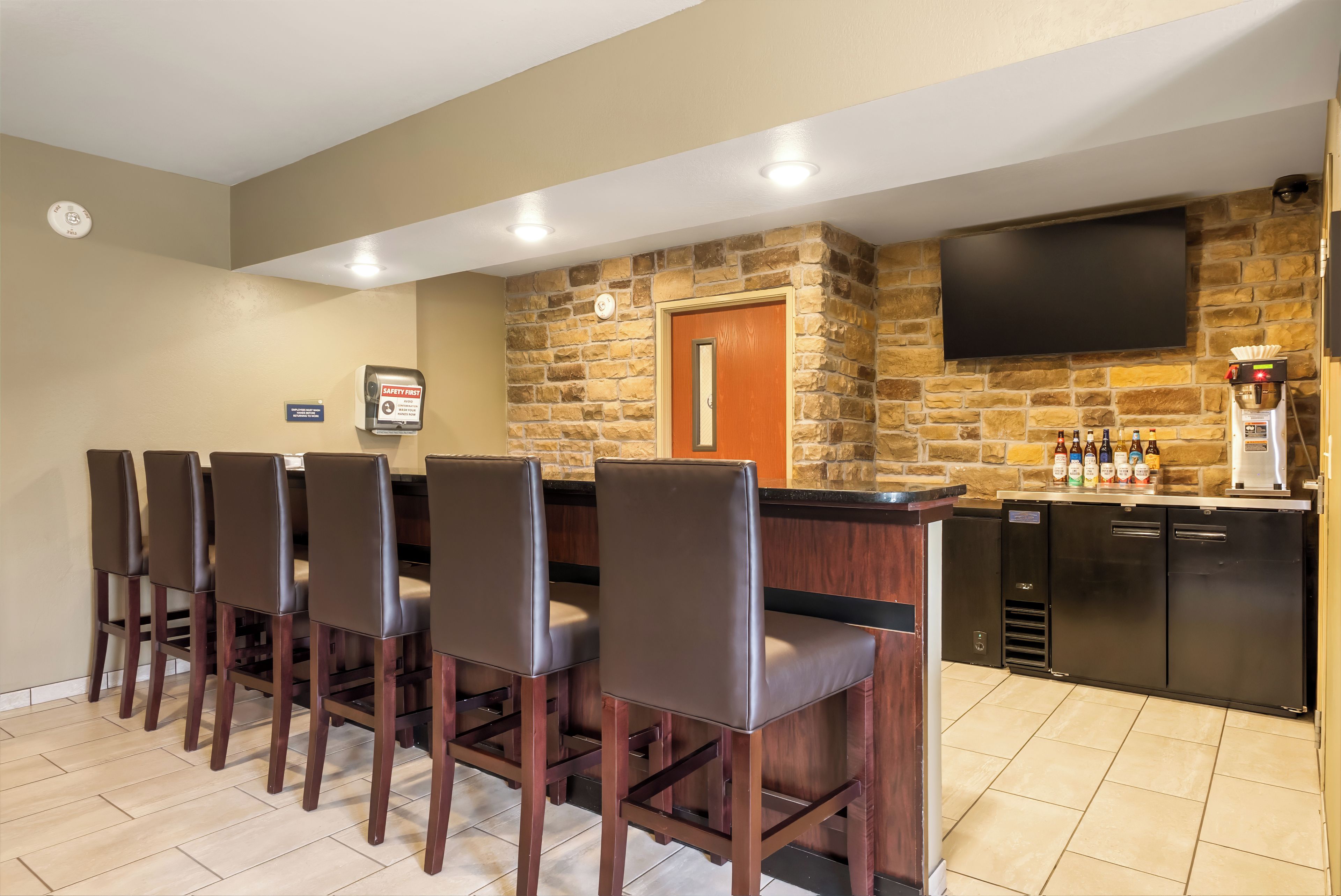 A bar area with a stone wall, a flat-screen TV, and a coffee machine.
