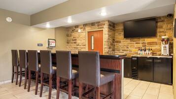 A bar area with a stone wall, a flat-screen TV, and a coffee machine.