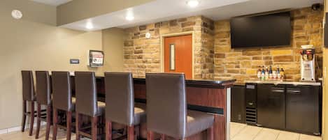 Un área de bar con pared de piedra, una televisión de pantalla plana y una cafetera.