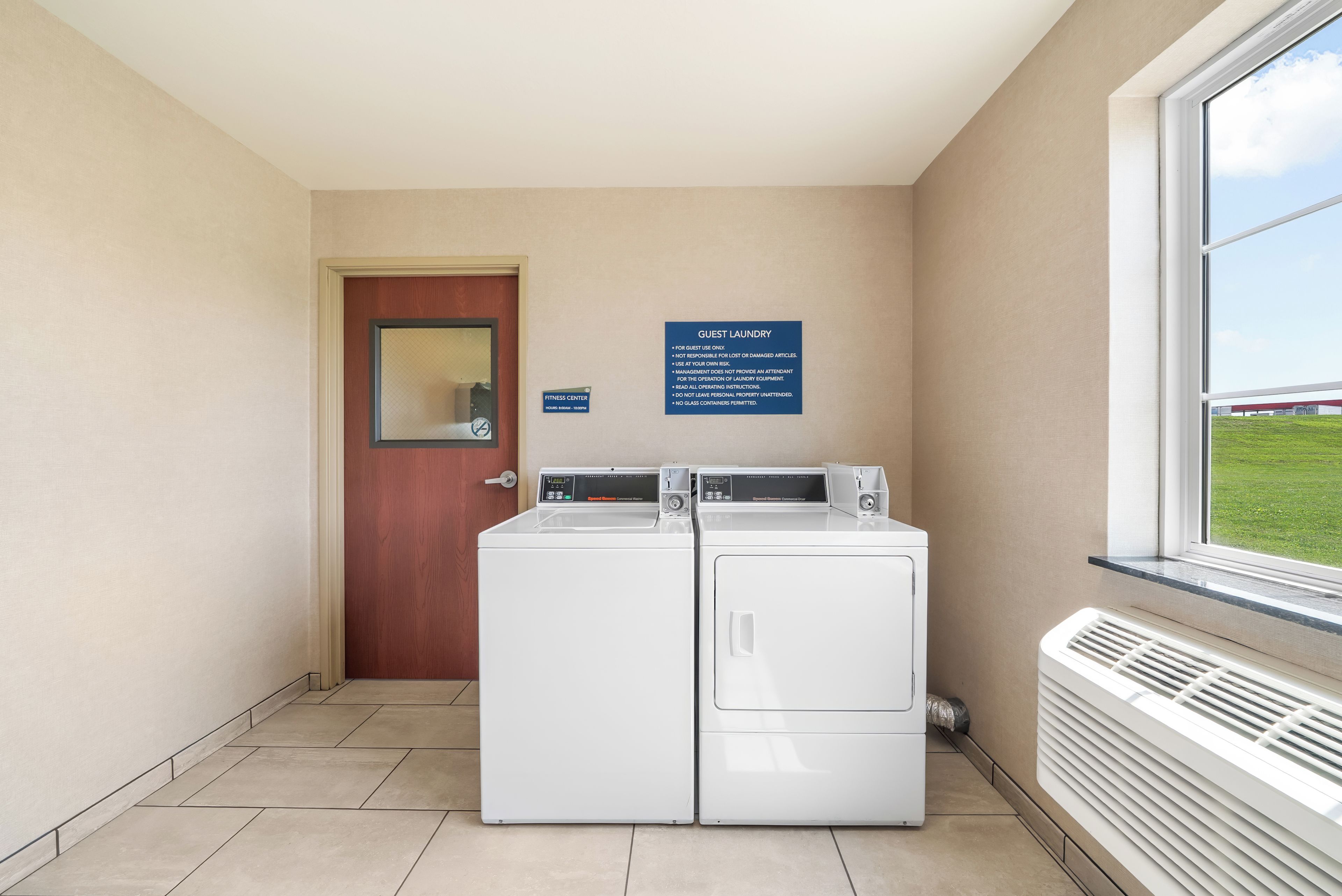 A laundry area with two front-loading washers and dryers, a door with a mirror, and a sign indicating guest laundry use.