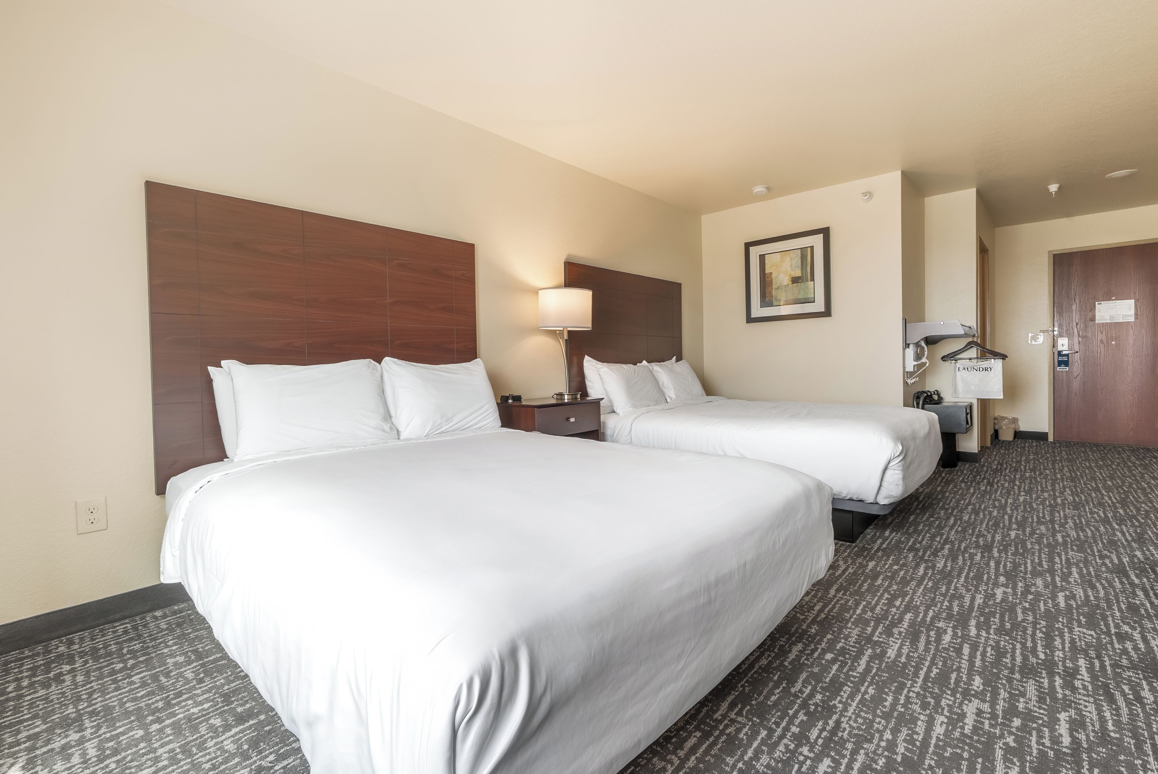A hotel room with two beds, a nightstand, a lamp, a painting, and a door with a sign.