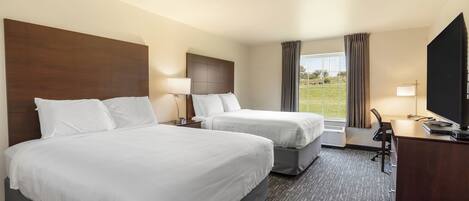 A hotel room with two beds, a desk with a flat-screen TV, and a large window with curtains.