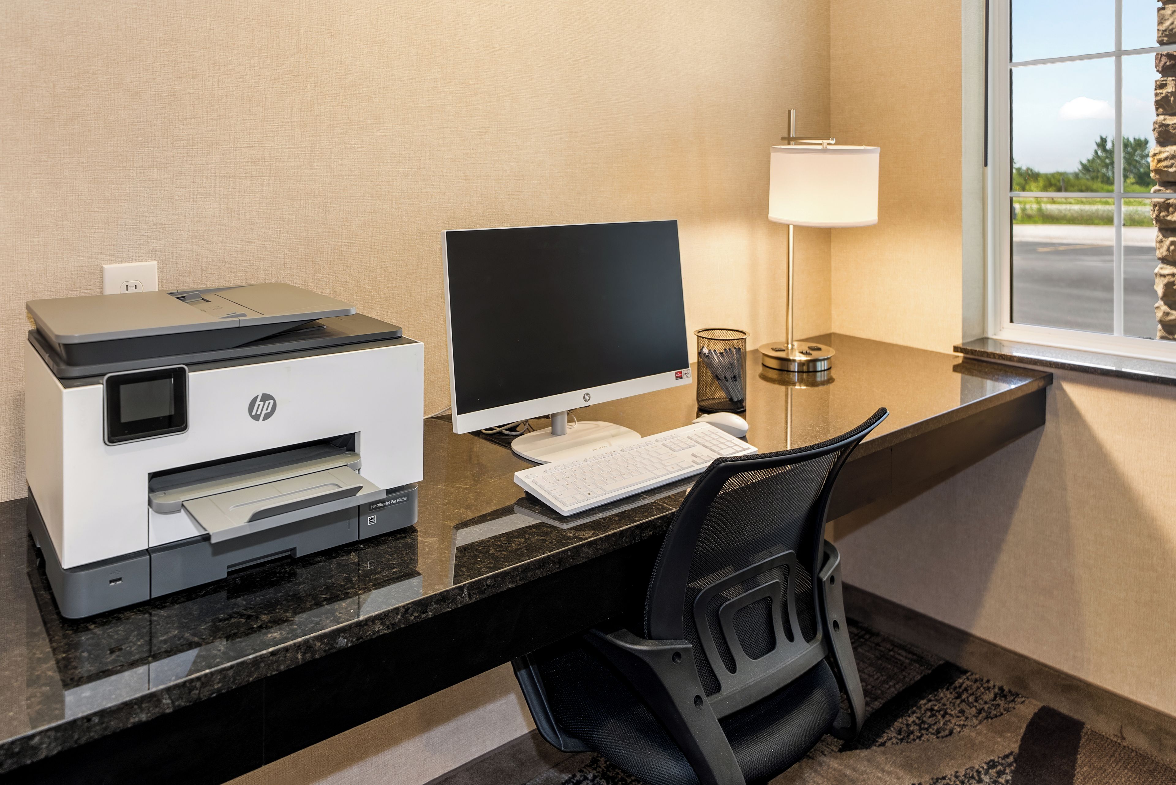 A hotel office with a desktop computer, HP printer, and a lamp.