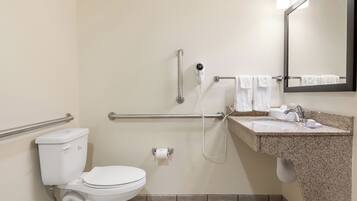 A bathroom with a toilet, grab bars, a hand dryer, a sink with a mirror, and a towel rack.