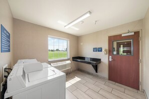 A hotel guest laundry area with a large window, a wall-mounted sink, and a door with a sign.