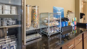 A breakfast buffet area with cereal dispensers, a coffee station, and packaged food items.