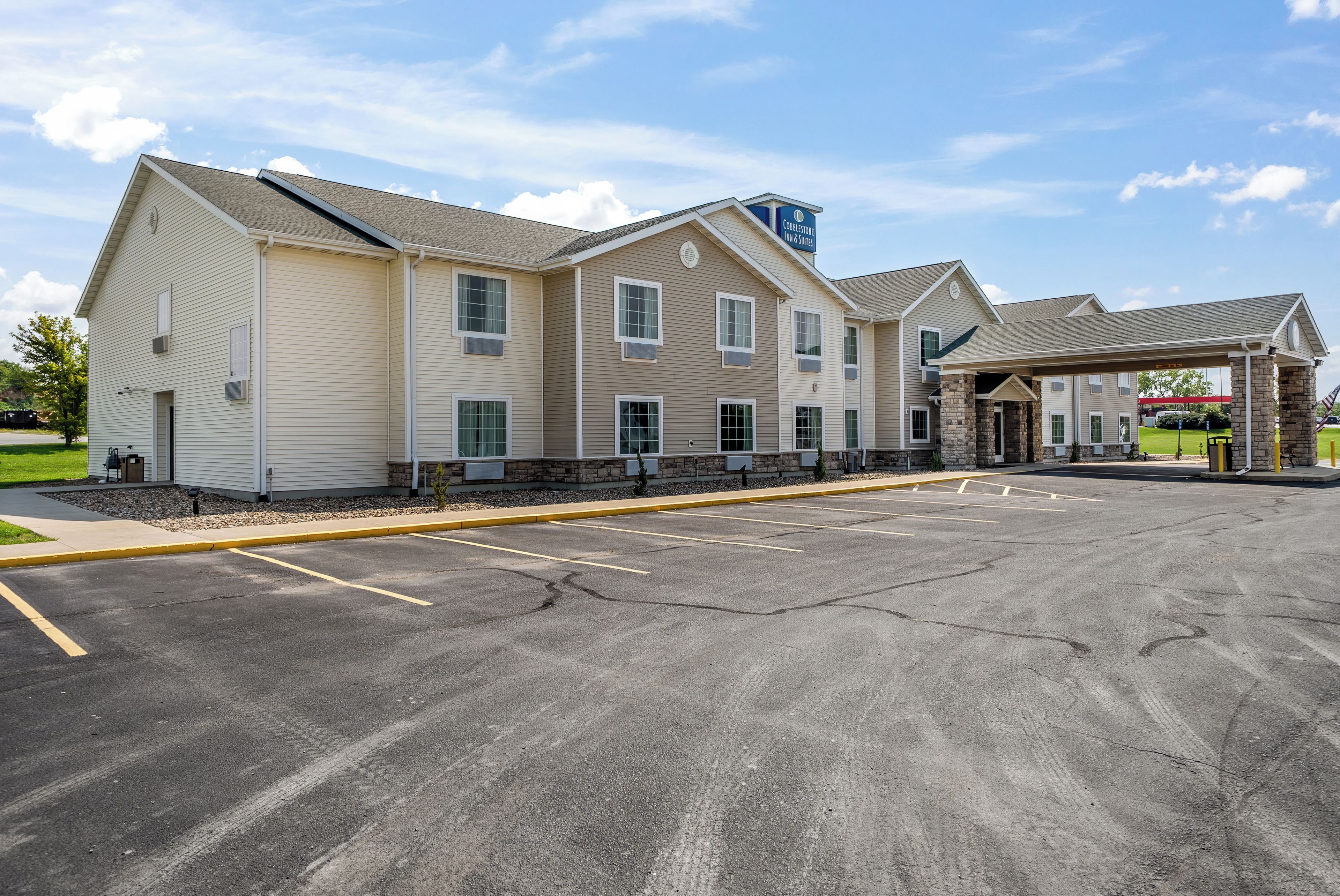 A hotel with a parking lot, a covered entrance, and a sign for Cobblestone Inn & Suites.