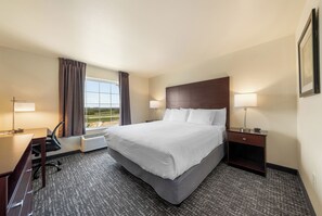 Una habitación de hotel con una cama grande, un escritorio con silla, una lámpara de escritorio, una mesita de noche con lámpara y una ventana con cortinas.