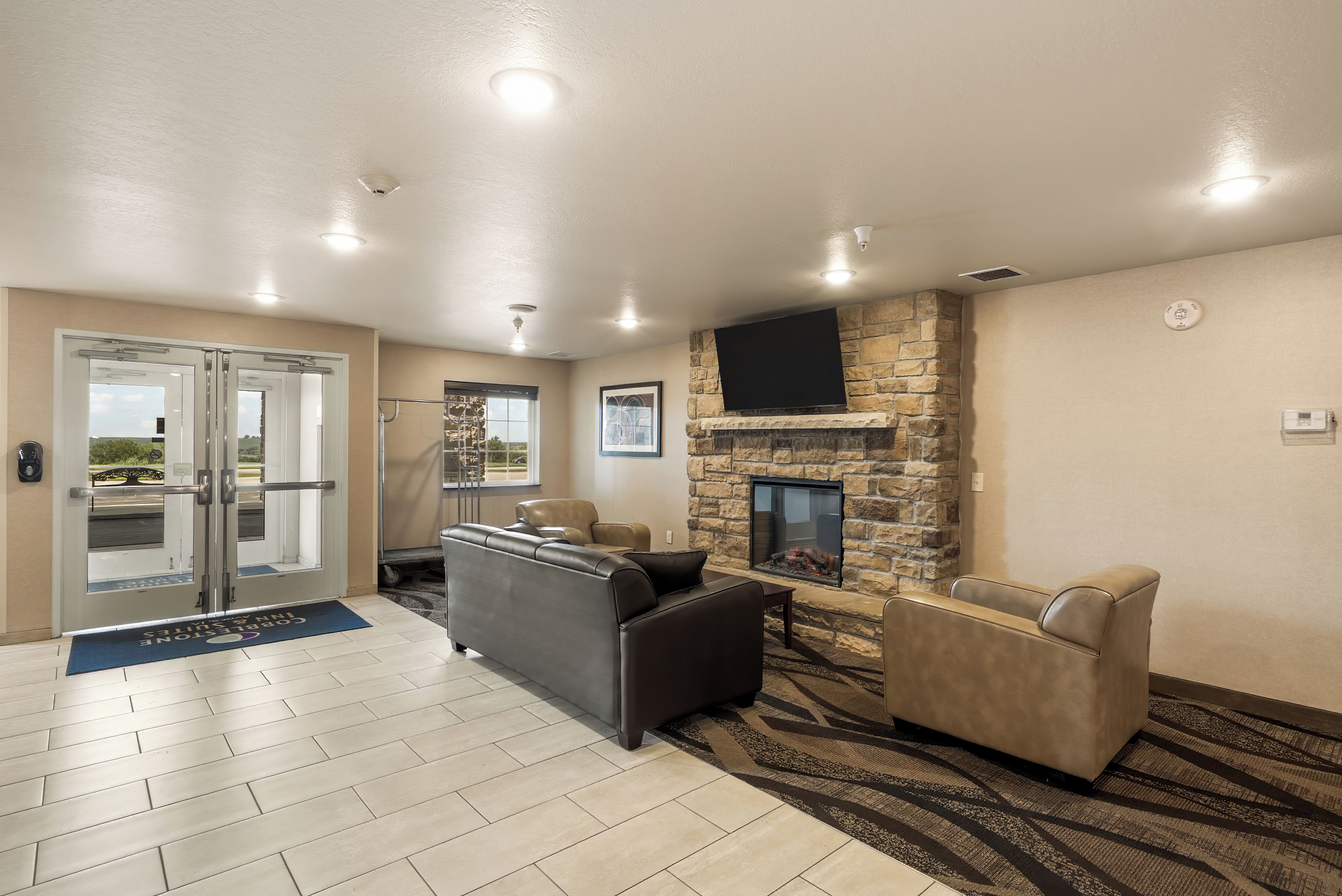A lobby with a stone fireplace, leather sofas, a flat-screen TV, and a door leading outside.