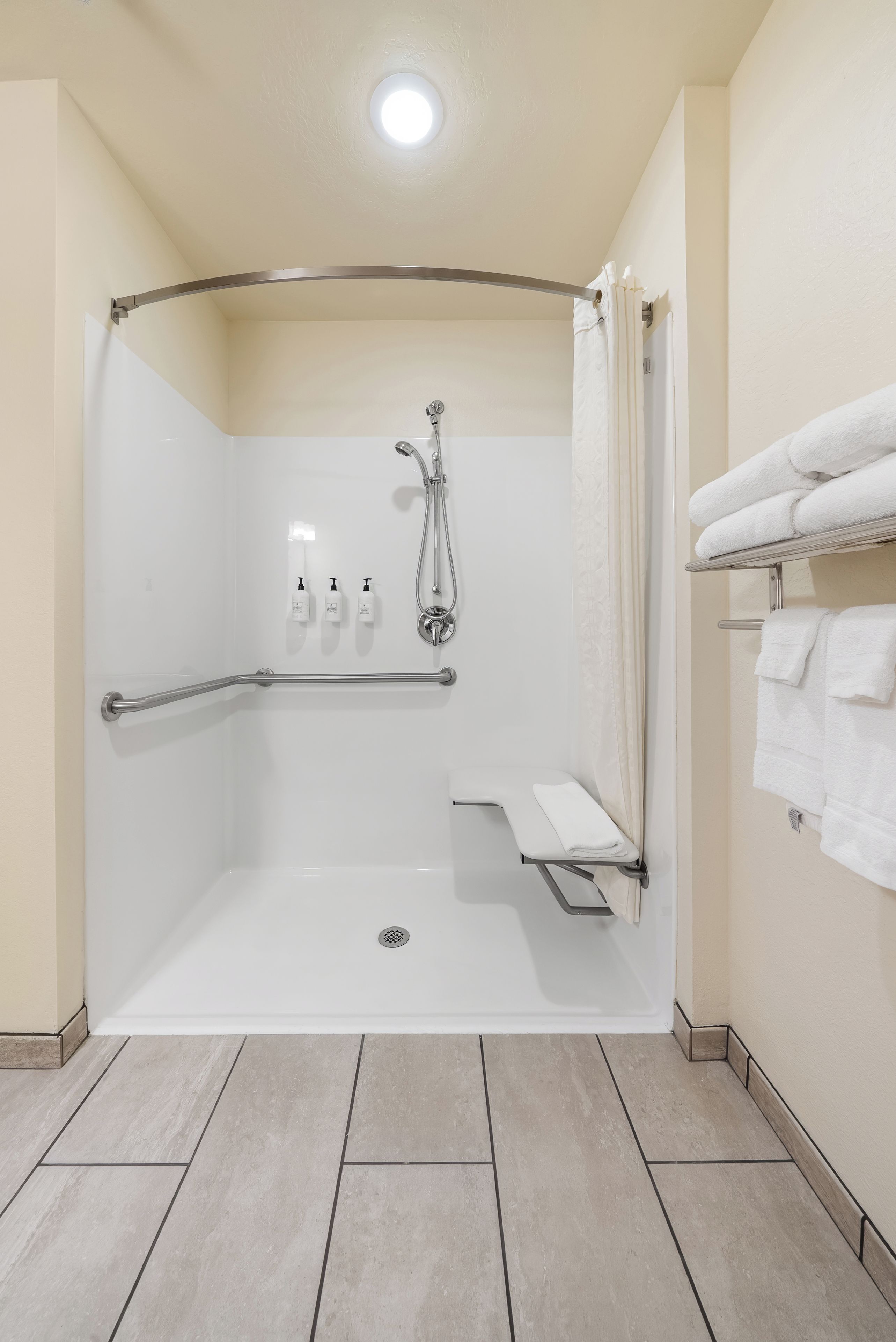 Un baño moderno con ducha a nivel, barras de apoyo, un asiento y un perchero para toallas.