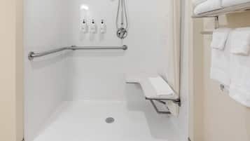Un baño moderno con ducha a nivel, barras de apoyo, un asiento y un perchero para toallas.