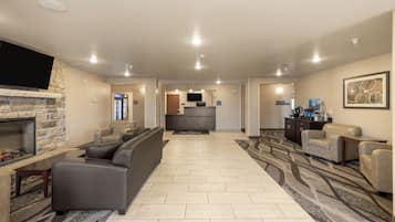 A spacious living area with a fireplace, leather sofas, a flat-screen TV, and a kitchen in the background.