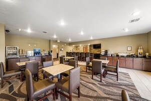Un comedor de hotel con varias mesas y sillas, una zona de cocina y un baño a la vista.