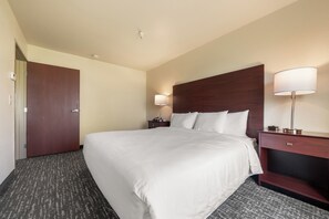 A hotel room with a large bed, two bedside tables with lamps, a wooden door, and a carpeted floor. - Cobblestone Inn & Suites - Avoca (Avoca)