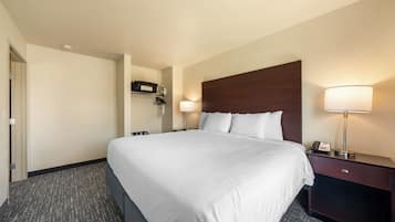 A hotel room with a large bed, two bedside tables, a nightstand, a lamp, and a wall-mounted shelf with a telephone.