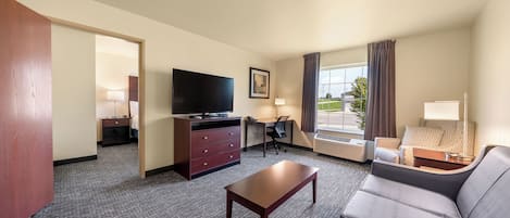 Habitación de hotel con televisión de pantalla plana, escritorio con silla, sofá y un amplio ventanal con cortinas.
