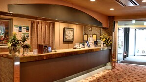 A reception desk with a curved design, informational posters, potted plants, and a framed artwork.
