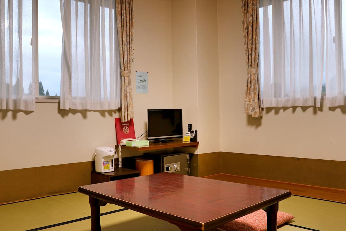 A room with tatami flooring, a wooden table, a television, and a safe.