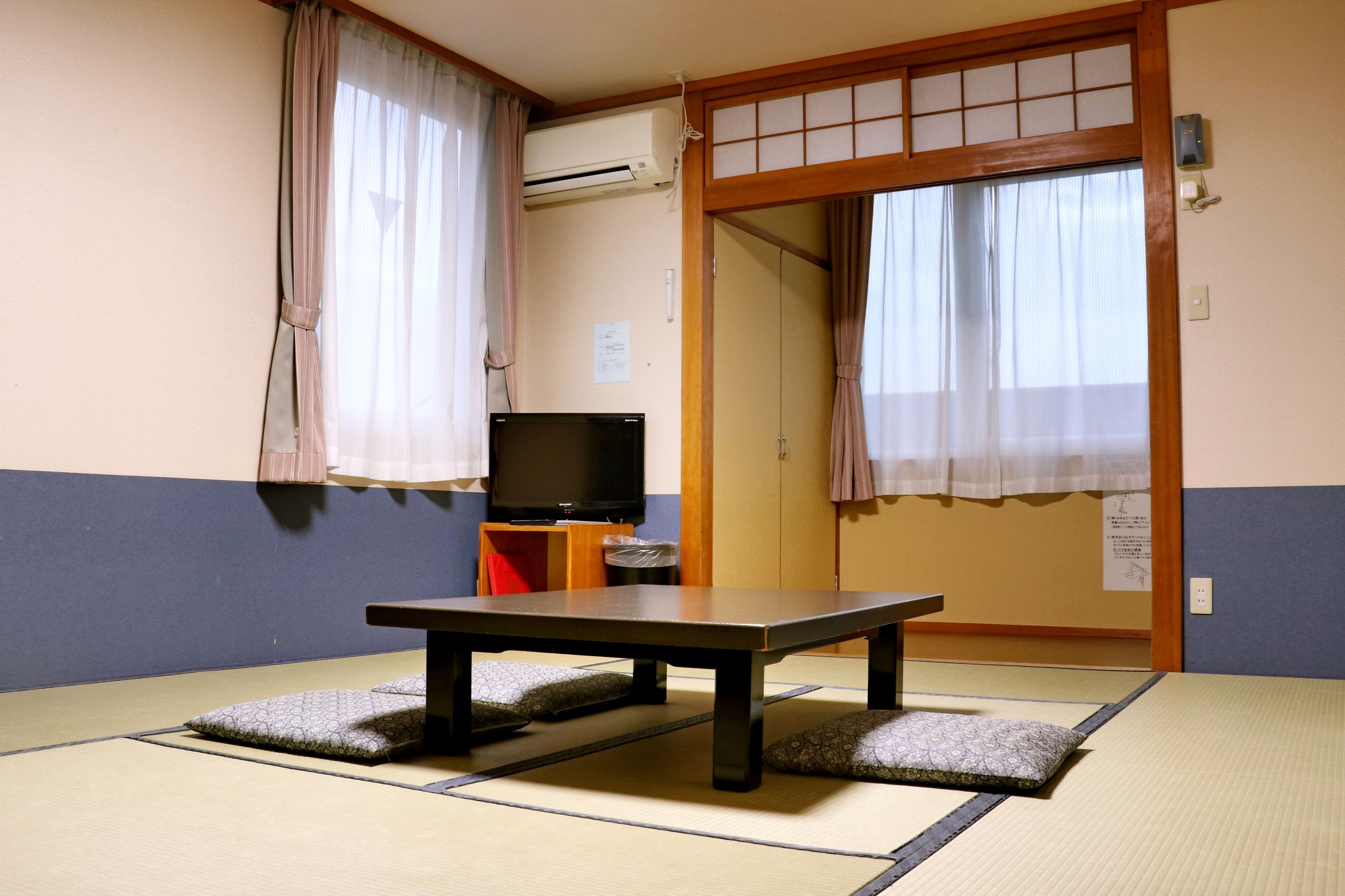 A traditional Japanese room with tatami flooring, a low table, a television, and sliding doors.
