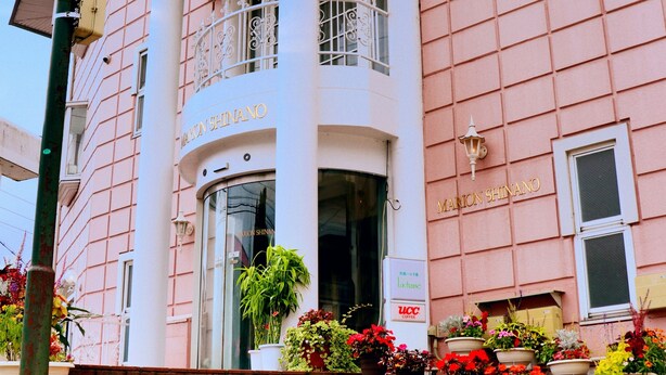A pink building with a white balcony and columns, a sign reading "MARTON SHINANO", and steps leading up to the entrance.