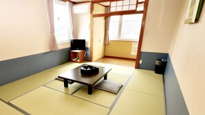A traditional Japanese room with tatami flooring, a low table with a black tray, a television on a wooden stand, and a sliding door.