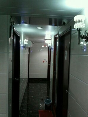 A hallway with a tiled floor, a trash bin, and a red mat at the end. - Marrigold Hostel (Kowloon)
