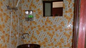 A bathroom with a floral tile wall, a white toilet, and a wooden basin sink. - New London Hostel (Kowloon)