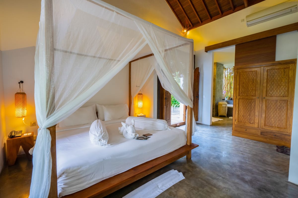 A large bed with a canopy, bedside lamps, and a wooden floor.