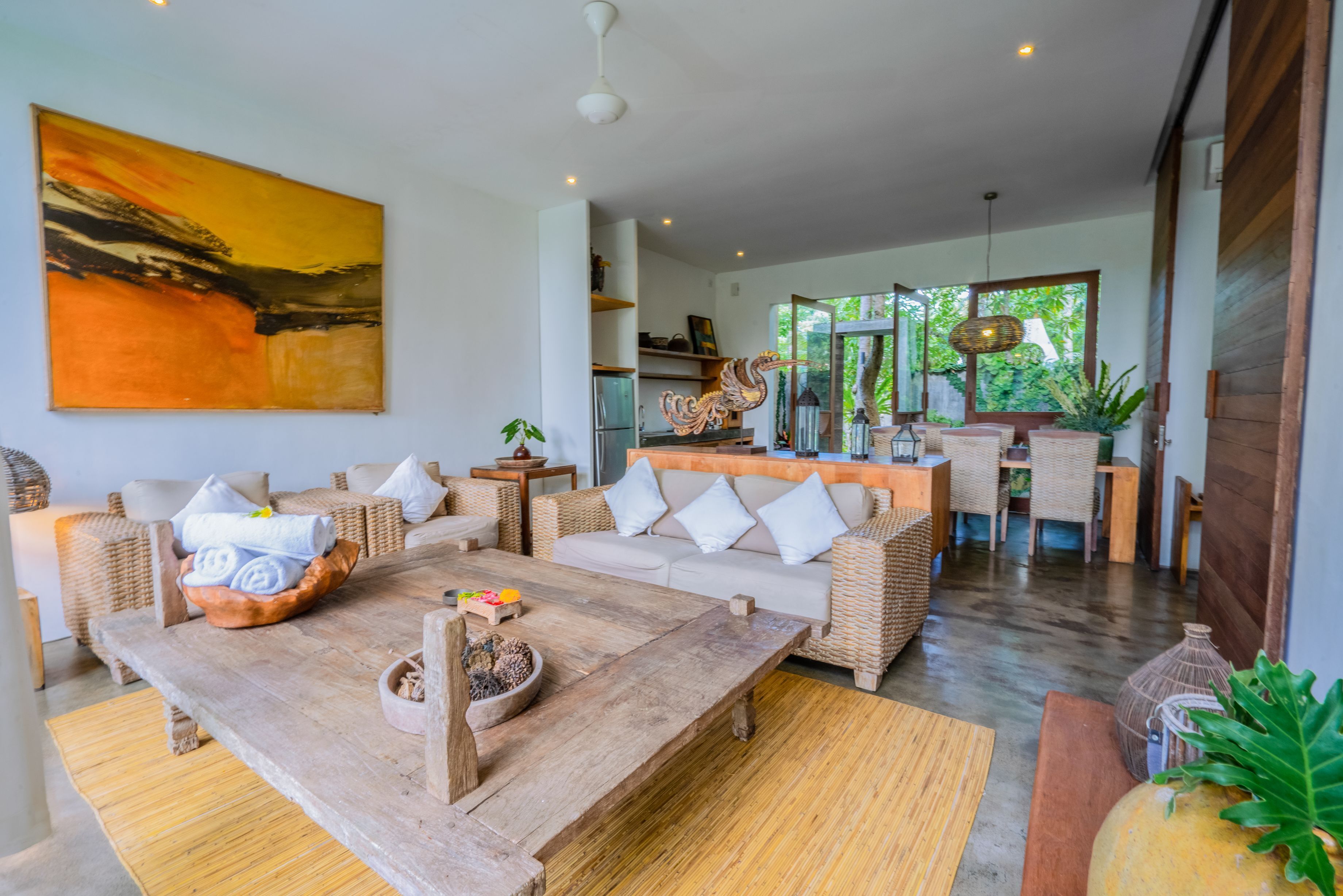 A spacious living area with a wooden coffee table, wicker furniture, and a large abstract painting on the wall.