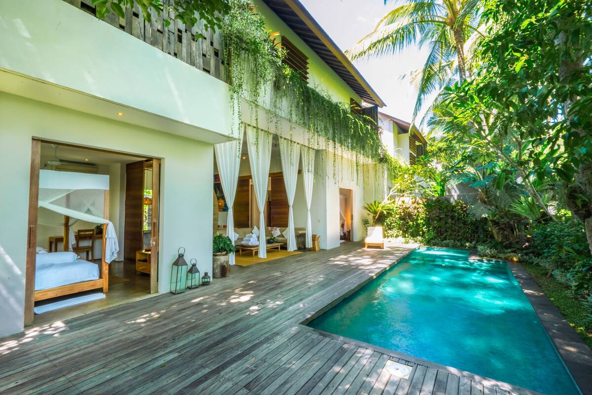 A modern resort with a wooden deck, a swimming pool, and rooms with large windows and curtains.