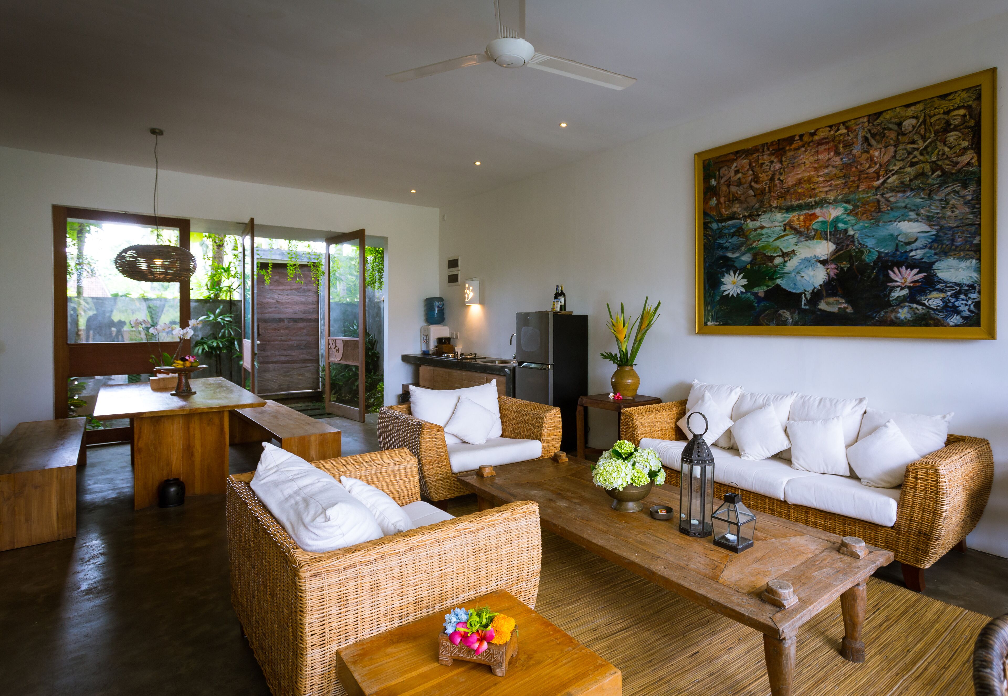 A spacious living area with wicker furniture, a wooden coffee table, and a large painting on the wall.