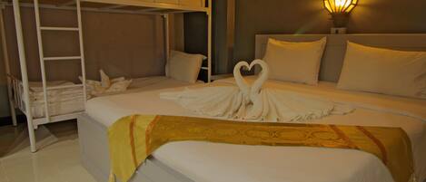 A hotel room with a bunk bed, a heart-shaped towel arrangement on the bed, and a wall-mounted lamp.