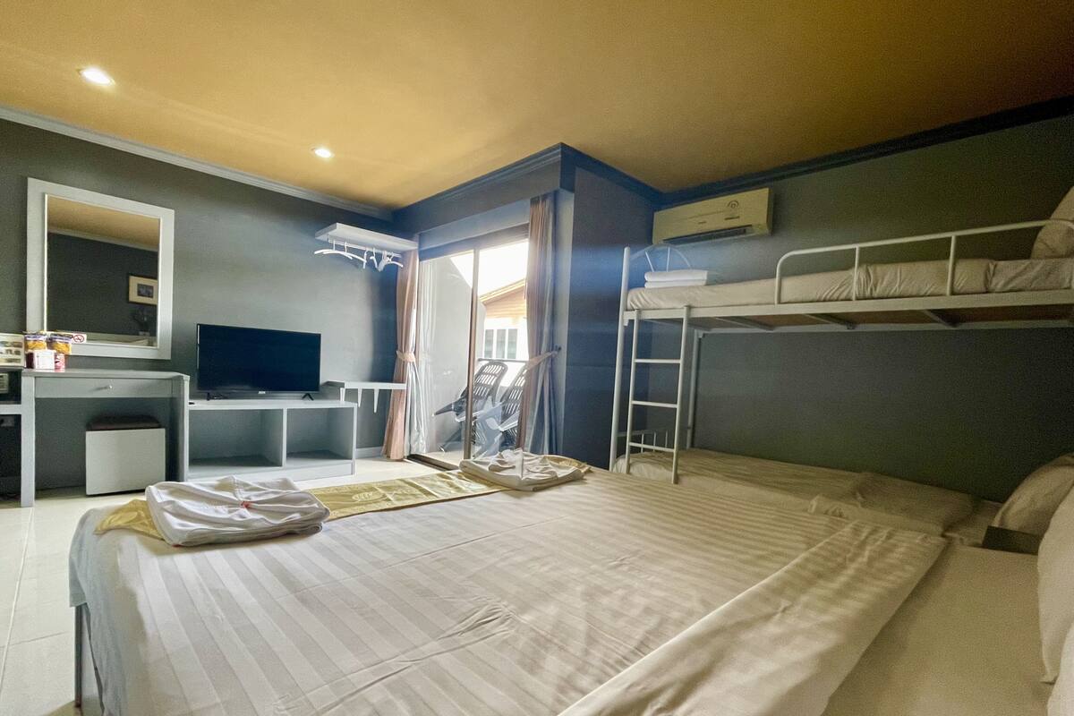 A hotel room with a large bed, a desk with a TV, a bunk bed, and a window with curtains.