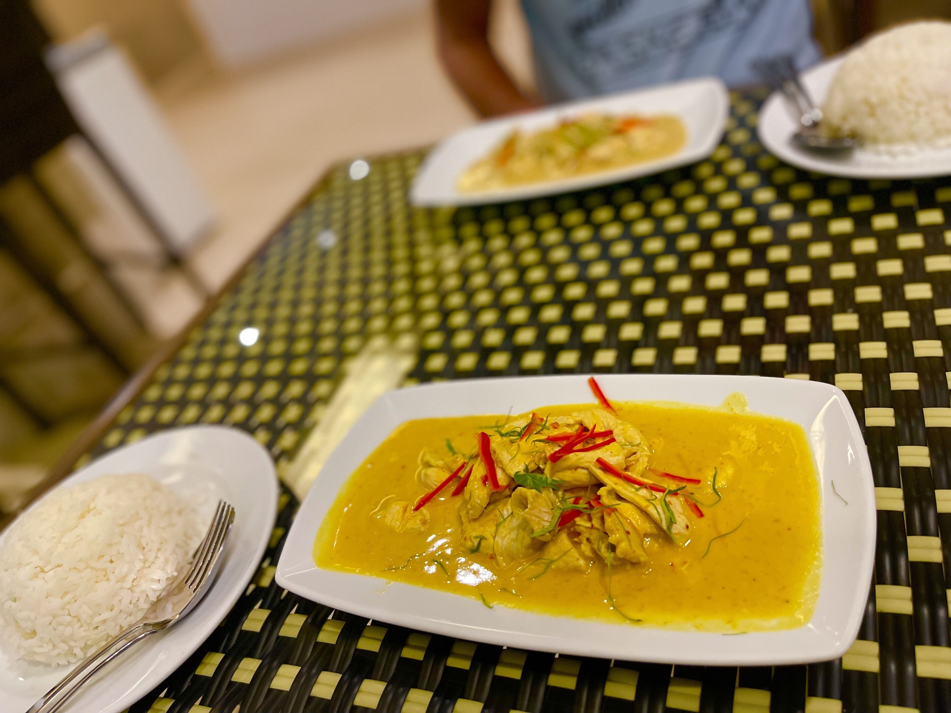 A table with a square plate of yellow curry and white rice, a fork, and a spoon.