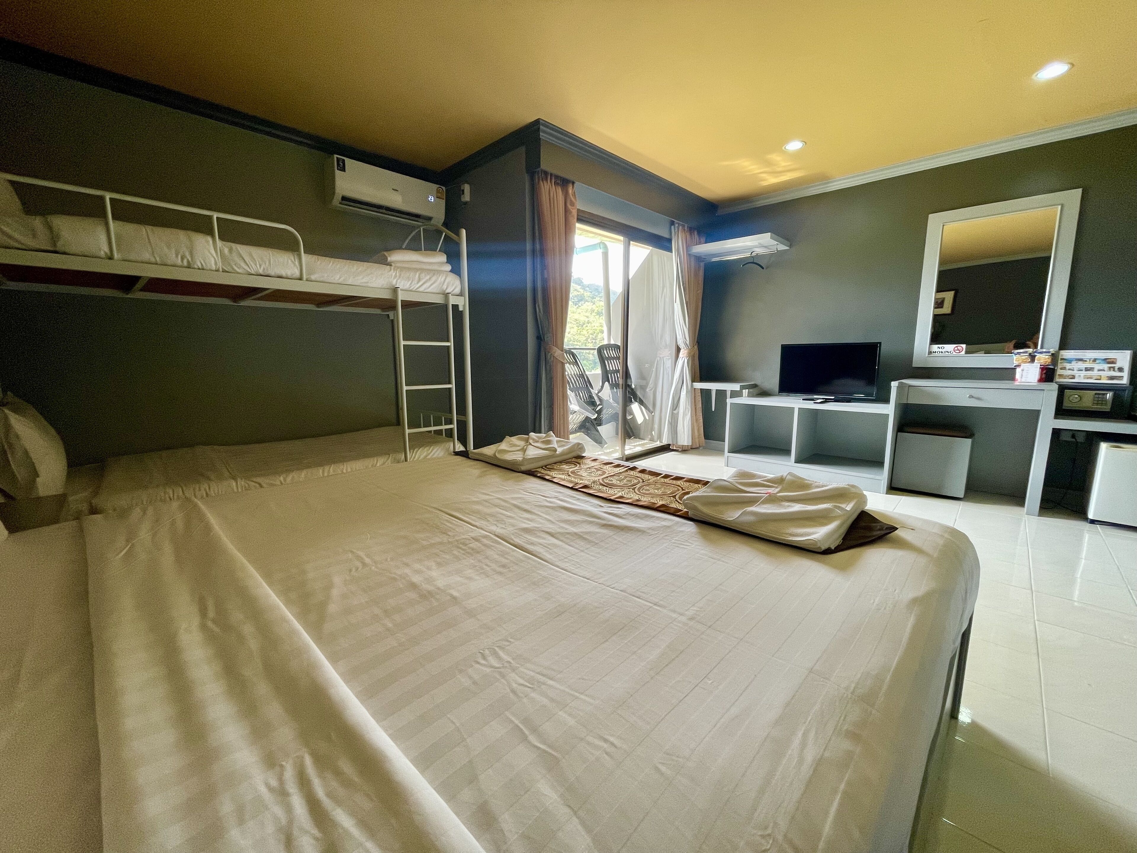 A hotel room with a bunk bed, a desk with a computer, a TV, and a mirror.